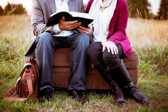 Paare - Ein paar sitzt gemeinsam auf einer Wiese und liest ein Buch.