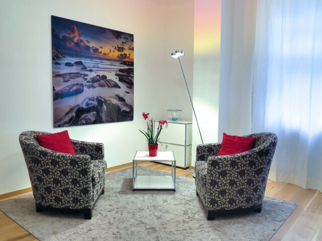 Psychotherapie - ein Behandlungszimmer mit zwei leeren Sesseln, Tisch und Bild an der Wand.